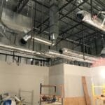 Exposed HVAC ductwork and piping in a Sierra Trading Commercial HVAC Spokane Valley project, with unfinished walls, scaffolding, and construction materials visible.